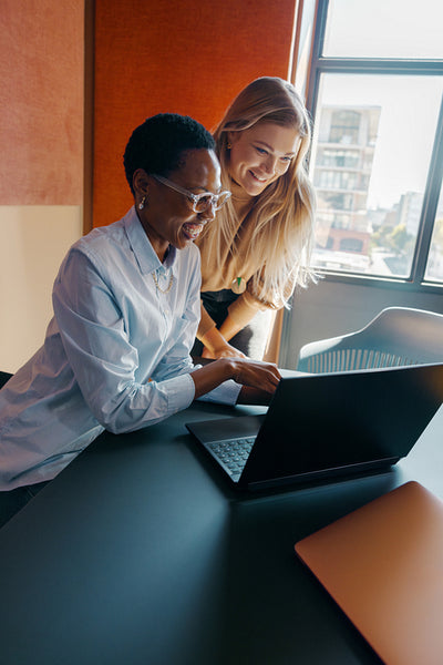 Two women working together on a laptop in a modern office setting