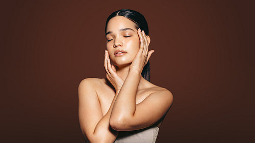 Beautiful young woman touches her flawless skin in a studio