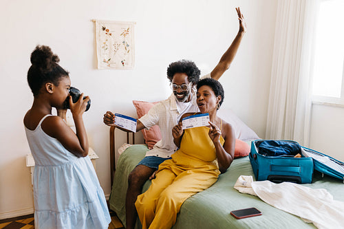 Young daughter taking a picture of her parents holding flight tickets with a camera