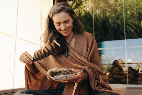 Cheerful senior woman holding a sage smudge stick and a feather