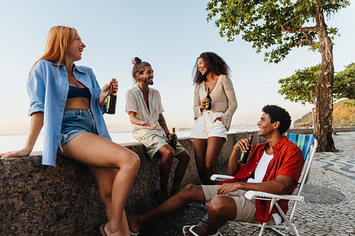 Group of young adults sitting outdoors at sunset with drinks