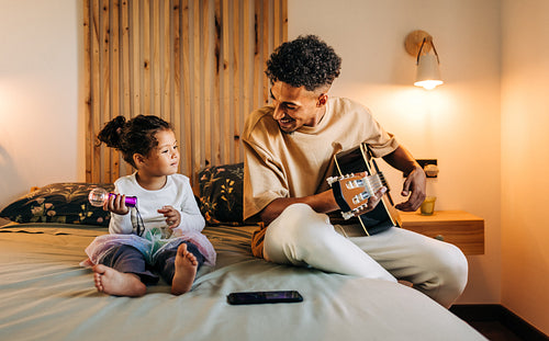 Happy single father playing a guitar for his daughter at home