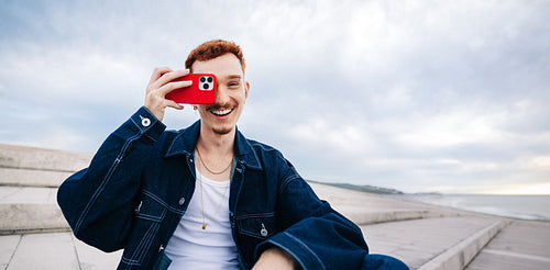 Young man taking photograph with smartphone by the sea