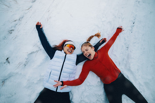 Happy women laugh while making snow angels after winter training