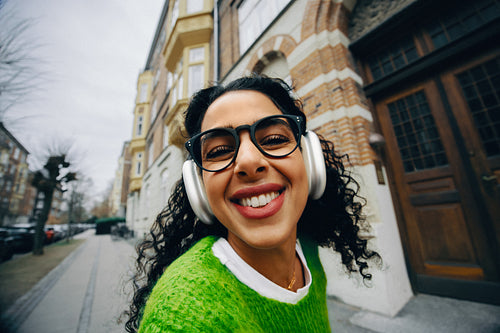 Her selfie catches the woman smiling with headphones and music on a city walk