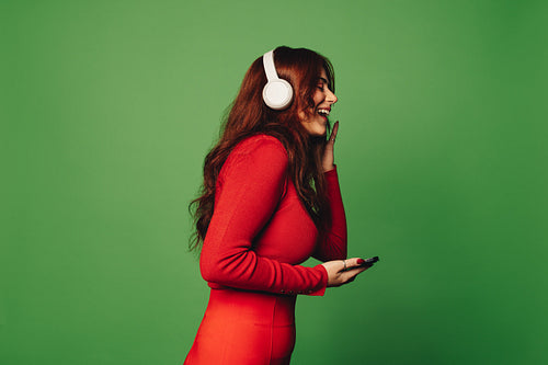Young woman listening to music with wireless headphones and a smartphone on a green background