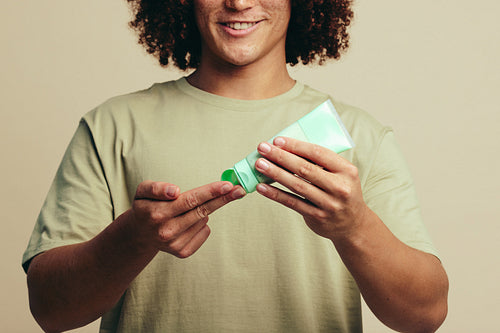 Happy young man applying a facial mask on his fingers, starting his skincare routine