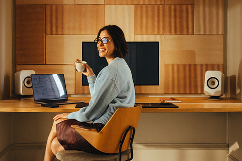Smiling woman enjoys coffee while working at a desk in her home office