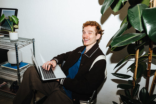 A freelance workday keeps a young man smiling with his laptop at home.