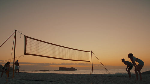 Mixed doubles: Athletes playing beach volleyball as the sun sets