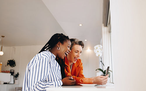 Happy business women laughing excitedly while using a smartphone together in a cafe
