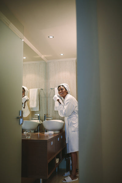 Female in bathrobe wiping her face with towel in bathroom
