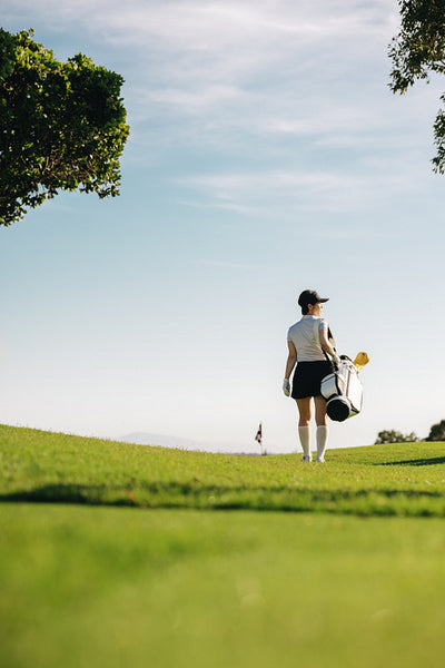 Female golfer carrying a golf bag as she walks from the green on a scenic golf course under clear sky