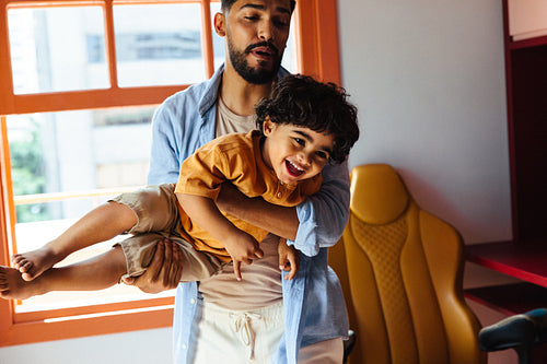 Father playing joyfully with his young son in a colorful home setting