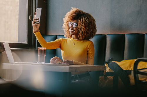 Smiling female traveller sitting at a coffee shop taking selfie
