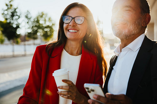 Professional colleagues enjoying outdoor discussion with coffee under sunlight