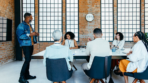 Mature businessman presenting to diverse colleagues in a well-lit, contemporary meeting space