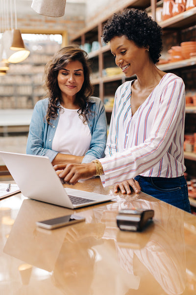 Female entrepreneurs using a laptop together in their ceramic store