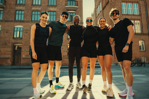 Running friends in fitness group posing together outdoors after urban run club workout
