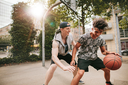 Two young friends playing basketball on court outdoors