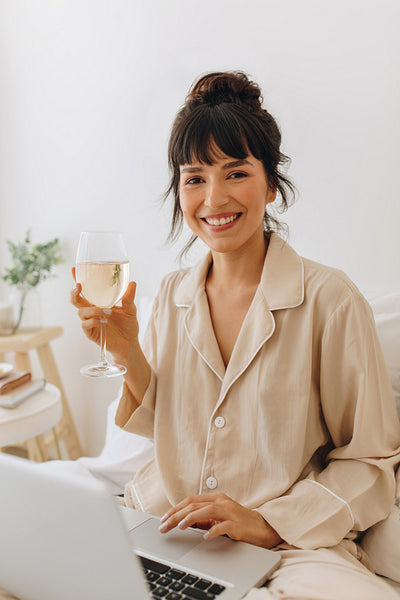 Portrait of smiling woman using laptop at home and enjoying wine