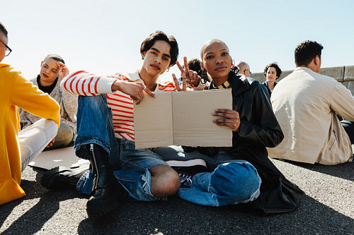 Two protestors holding a blank sign while sitting amidst a crowd outdoors