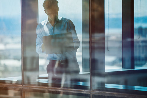 Businessman standing inside office building and using laptop