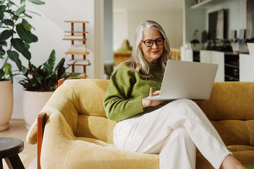 Senior woman uses a laptop while sitting on a sofa at home