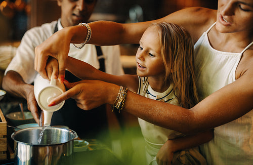 Mother helping child pour liquid during a cooking lesson