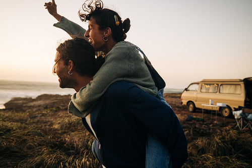 Joyful couple share a playful piggyback at sunset by the coast