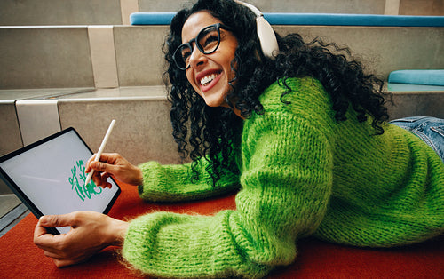 Happy digital artist designs in library with tablet and stylus