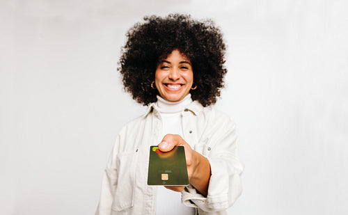 Happy woman with curly hair holding out her credit card in a studio