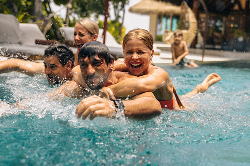 Family enjoying a fun pool race on vacation with laughter and splashing water in a tropical resort setting