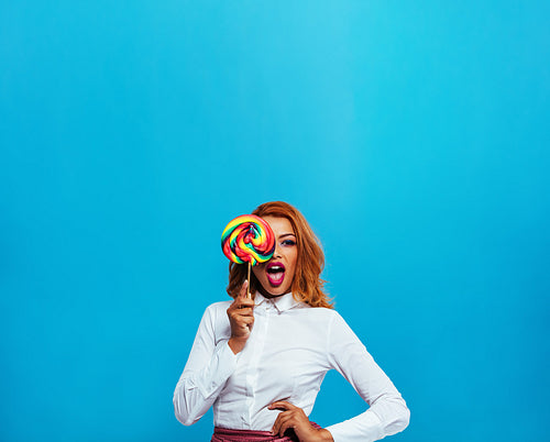 Beautiful young woman covering her eye with lollipop 