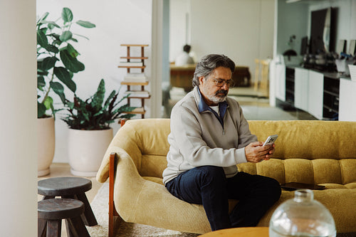 Senior man uses smartphone while relaxing on sofa at home