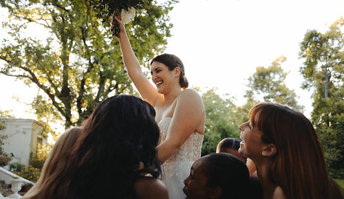 Bride celebrating joyously surrounded by friends at outdoor wedding reception