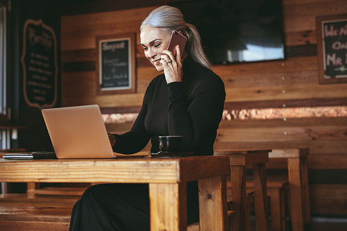 Businesswoman at cafe making a phone call and using laptop