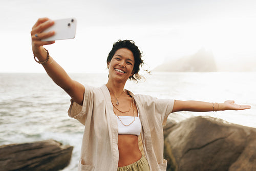 Carefree woman posing for a selfie at beach during holiday, smiling and waving