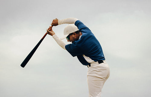 Male baseball batter wearing sunglasses and a hat prepares for a powerful swing