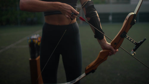 Young woman practicing archery with focus and joy outdoors at golden hour