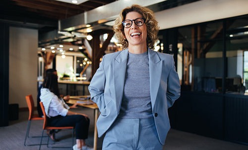 Woman standing in an office, she is smiling and wearing a suit