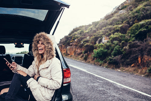 Woman sitting in the car trunk with a smart phone