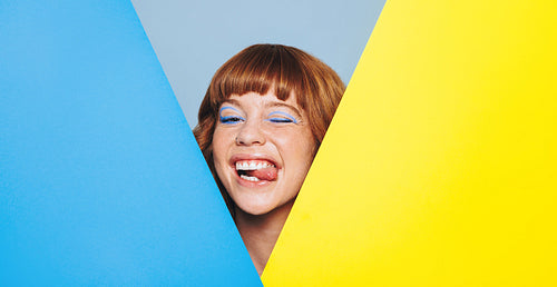 Quirky young woman sticking her tongue out from behind two colour placards