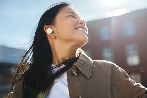 Young woman smiling with earbuds outdoors on a sunny street
