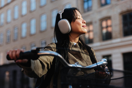 Woman on bicycle wearing headphones and enjoying sunlight