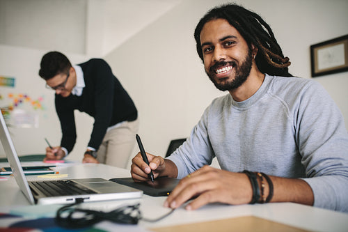 Smiling businessman working in office on a laptop using a digital writing pad.