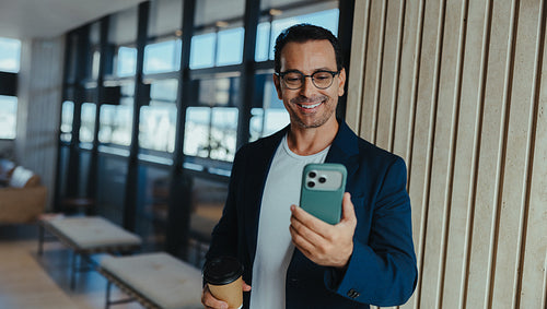 Businessman checks his phone with coffee in a modern office lobby