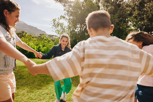 Children holding hands in a circle outdoors on a sunny day
