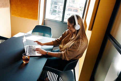Woman wearing headphones working on a laptop in a bright modern room