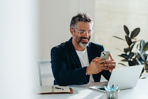 Focused professional man smiling at smartphone in bright modern office
